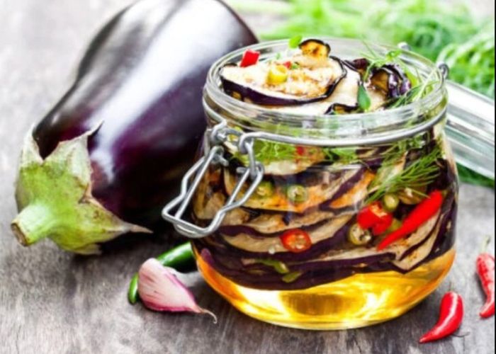 Frasco de vidrio con berenjenas al escabeche, laurel y granos de pimienta