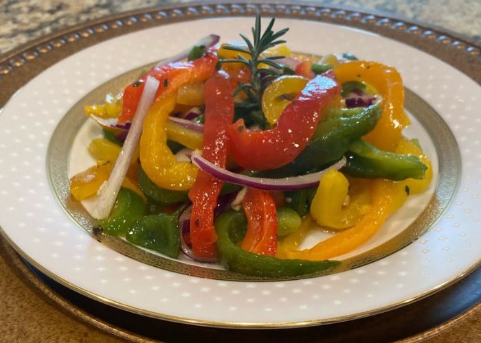 Tiras de morrón asado de colores rojo y amarillo en una fuente con ajo picado y aceite de oliva