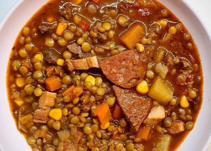 Olla rústica con guiso de lentejas humeante, zanahorias y perejil fresco