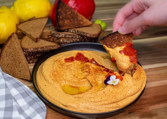 Cuenco de hummus color naranja intenso decorado con aceite de oliva y trozos de morrón asado