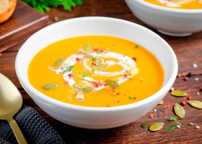 Plato hondo con crema de calabaza color naranja intenso decorada con semillas y una pizca de pimienta