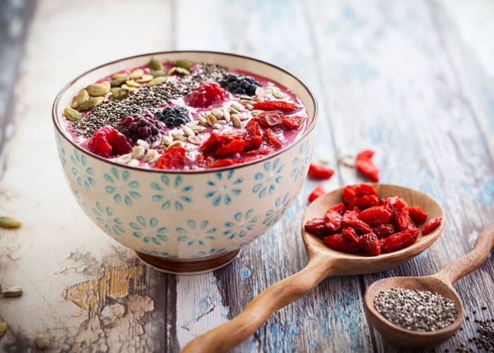 Bowl de cerámica con puré de frutas morado, decorado con quinua pop, plátano y semillas