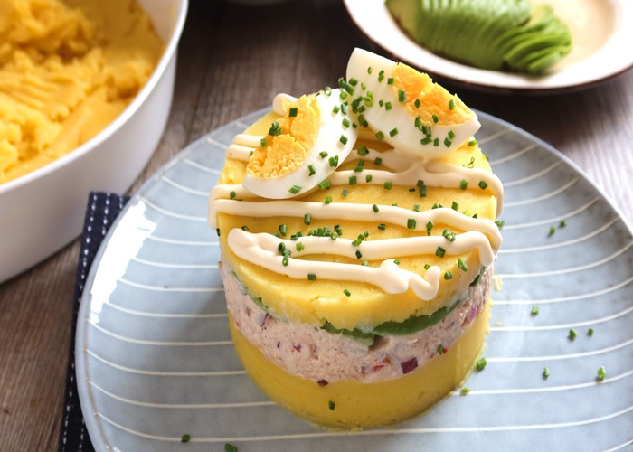 Causa limeña emplatada en capas con palta, pollo y decoración de huevo