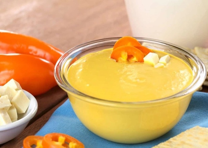 Salsa huancaína color amarillo vibrante en pocillo de cerámica con ajíes amarillos frescos al lado